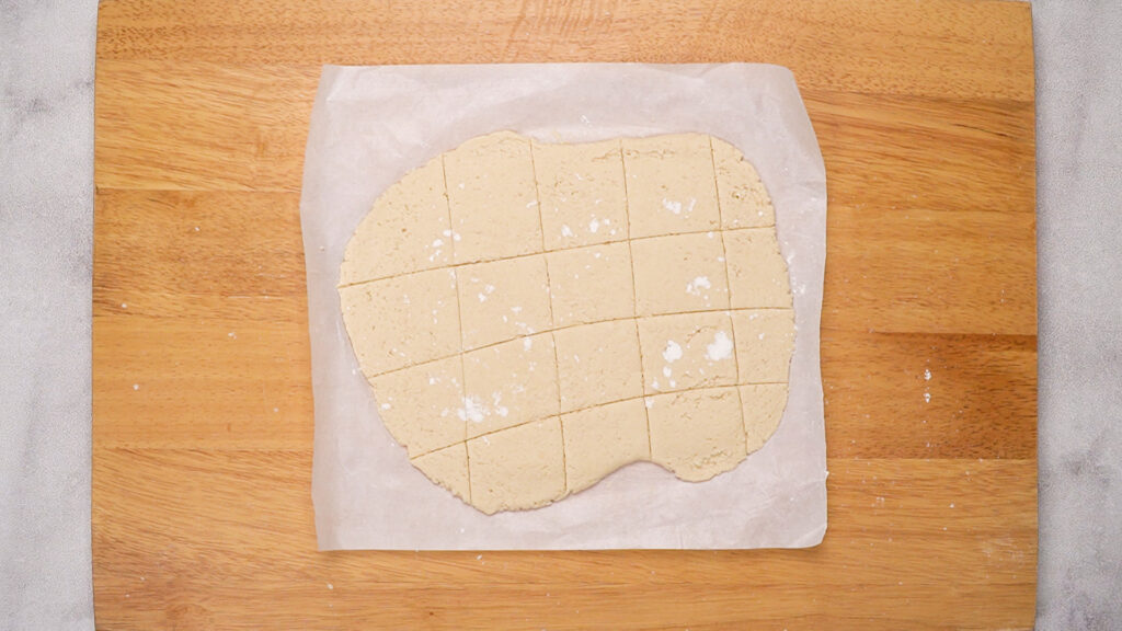 Rolled dough cut into even squares on parchment paper, ready for frying.