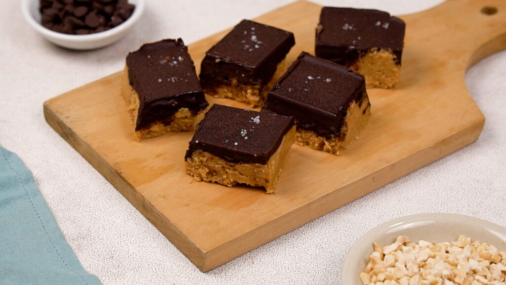 Close-up of several peanut butter chocolate bars on a wooden serving board, showing a thick peanut butter base and glossy chocolate topping.