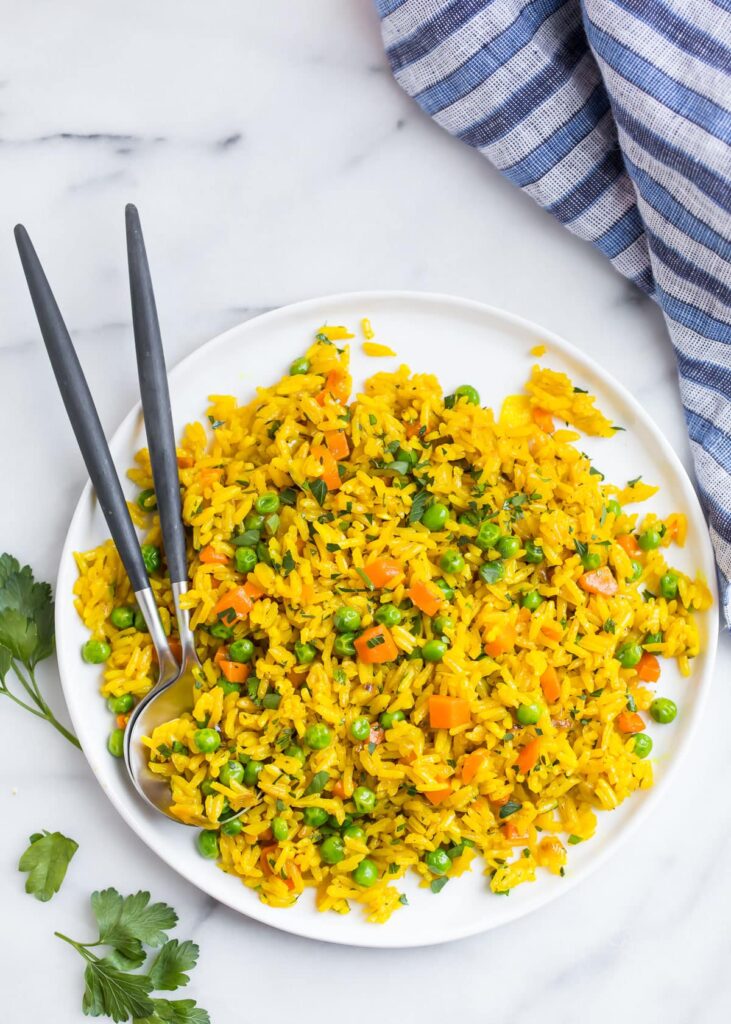 Turmeric rice in a white plate with serving spoons. Photo by wellplated.com.