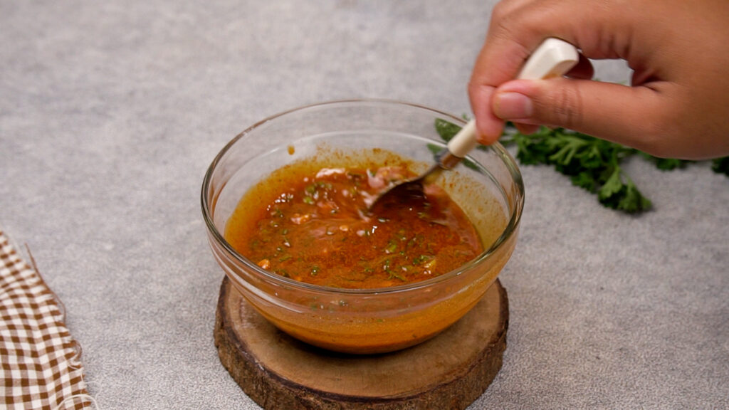A hand stirring together the melted butter, herbs, and spices in a bowl to make the cowboy butter sauce.