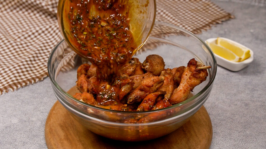 Golden fried chicken wings in a glass bowl with cowboy butter sauce being poured over them.