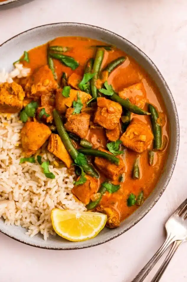 Butter chiken in a plate with rice and veggies.