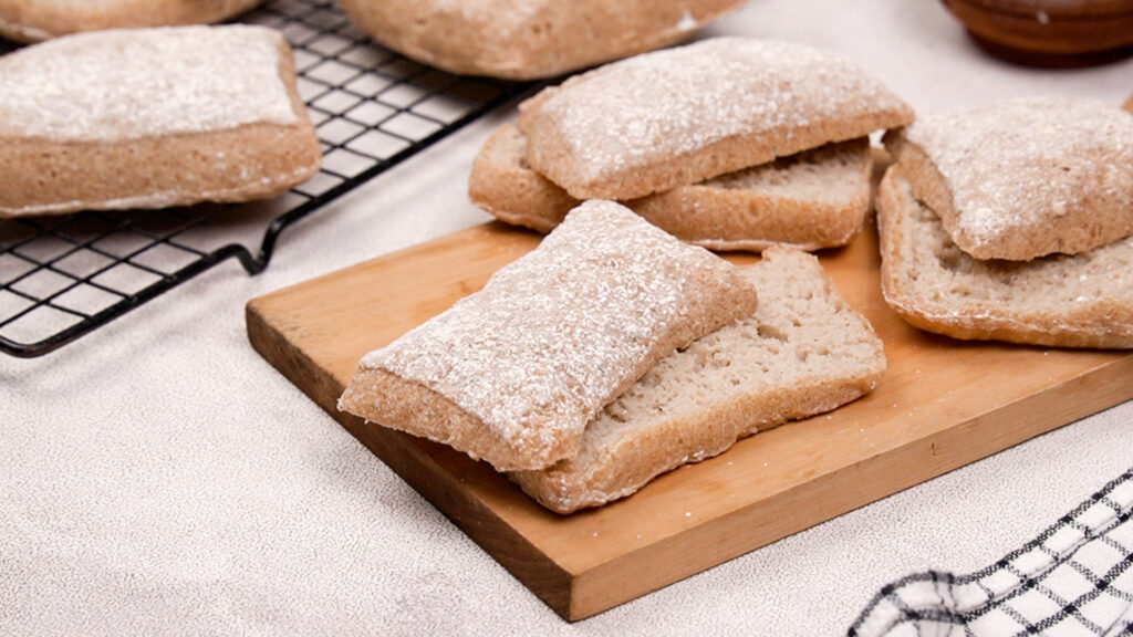 reshly baked gluten-free ciabatta rolls cooling on a wooden board and wire rack.