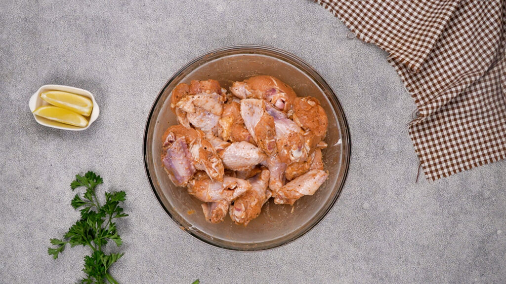 The chicken wings after being mixed with spices and cornstarch, evenly coated and marinating in the glass bowl.