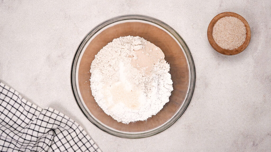 Overhead view of dry ingredients: Gluten-free flours, yeast, sugar, and salt. All in a glass mixing bowl.