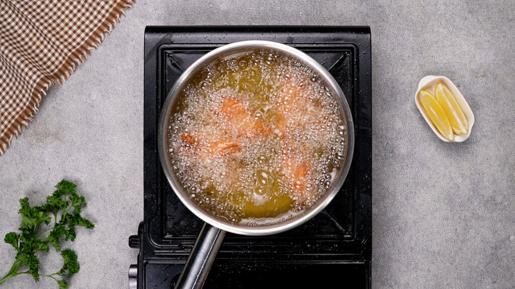 Chicken wings frying in hot oil in a deep pan, bubbles rising around the wings as they turn golden brown.
