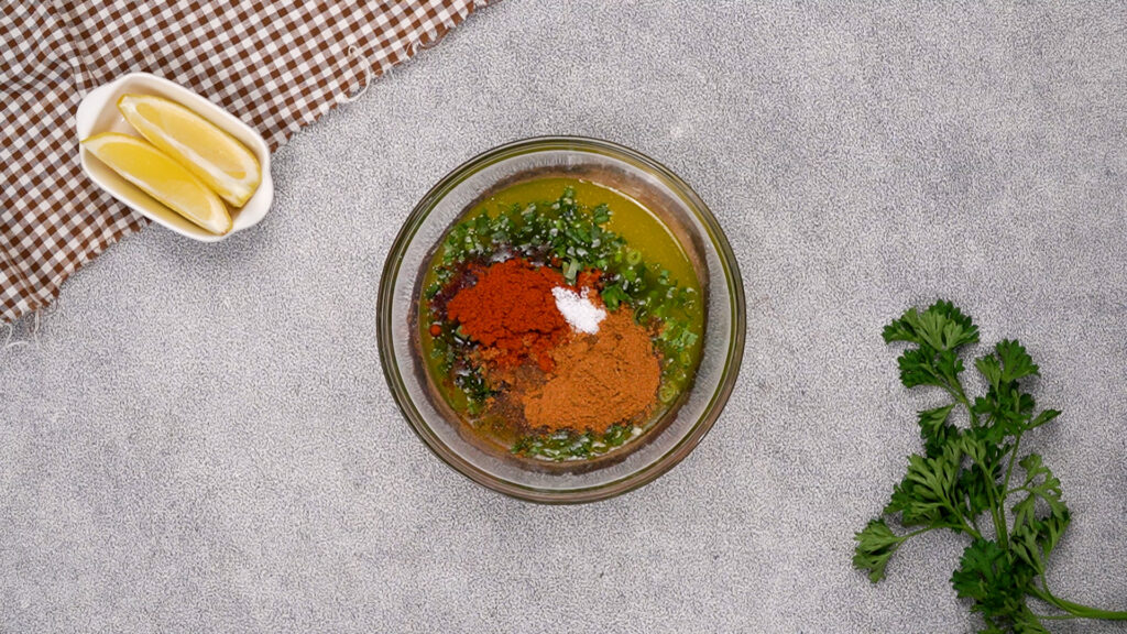 A glass bowl of melted butter with herbs, smoked paprika, cayenne, and salt on top, before being mixed into cowboy butter sauce.