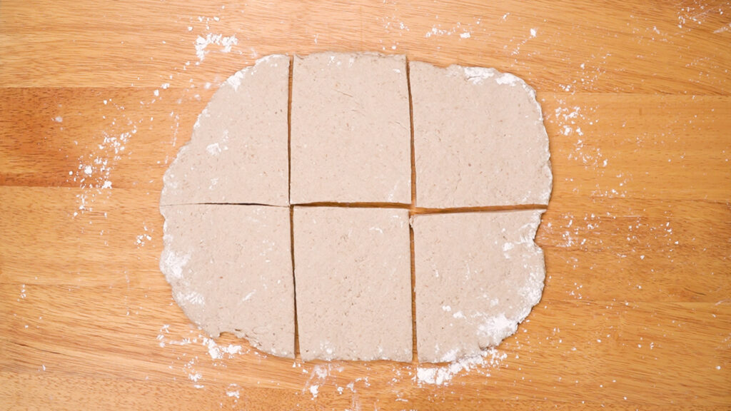 Flattened gluten-free ciabatta dough cut into six rectangular portions on a floured wooden board.
