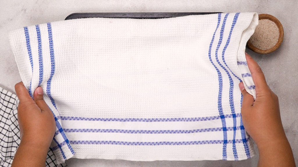 Dough portions covered with a white kitchen towel during the rising stage.
