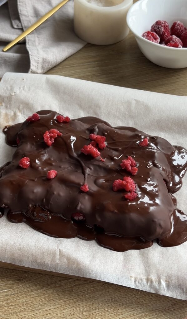 A layer of melted dark chocolate spread over white chocolate and raspberries, topped with small raspberry pieces.