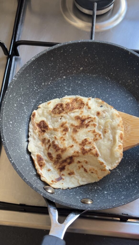 Almond flour tortilla cooking in a nonstick skillet with golden brown spots forming on the surface.