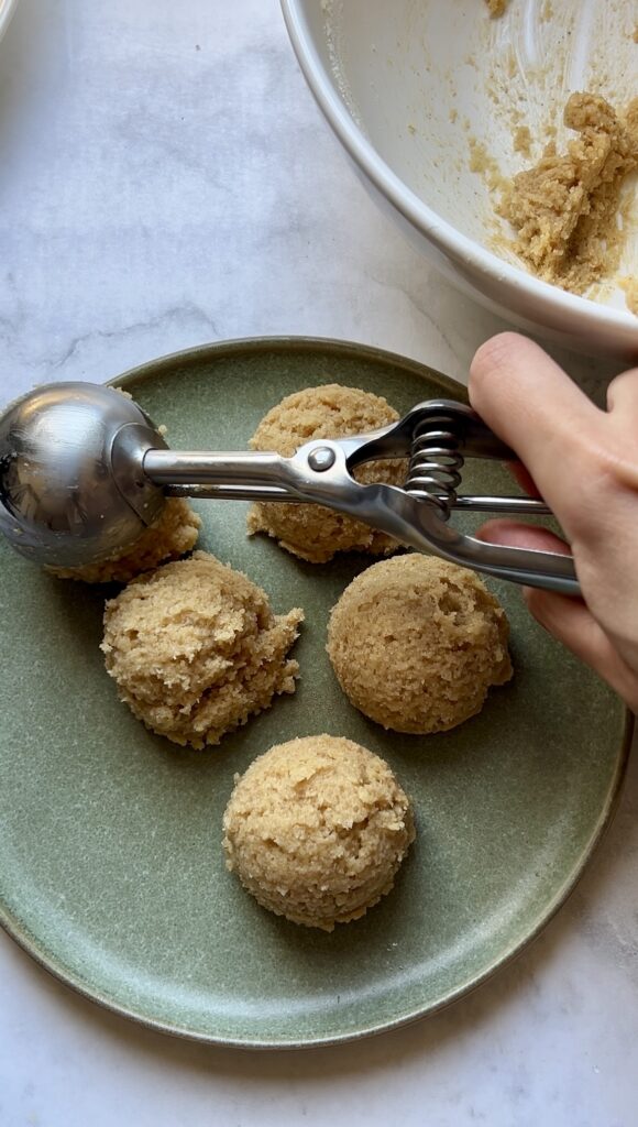 Cookie scoop portioning almond flour cookie dough onto a plate before baking.