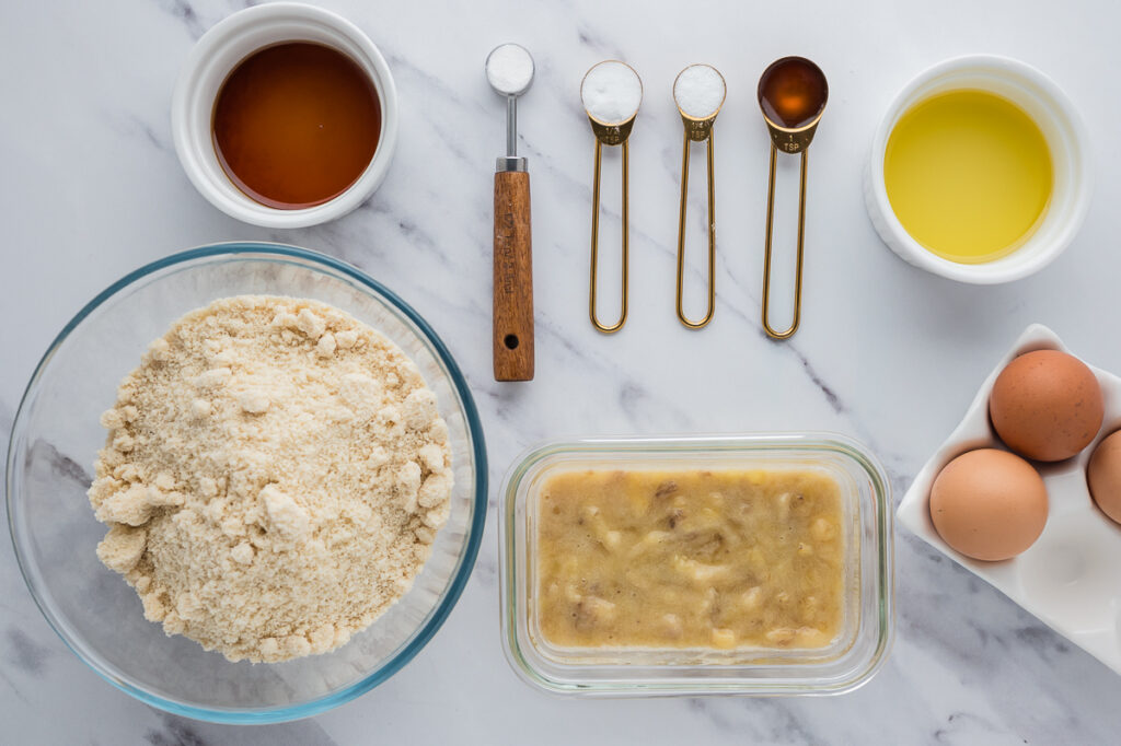 Almond flour banana bread ingredients arranged on a counter including ripe bananas, almond flour, eggs, and maple syrup.