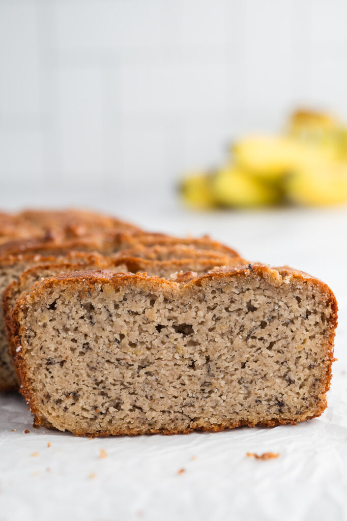 Sliced almond flour banana bread loaf showing soft moist crumb with ripe bananas in the background.