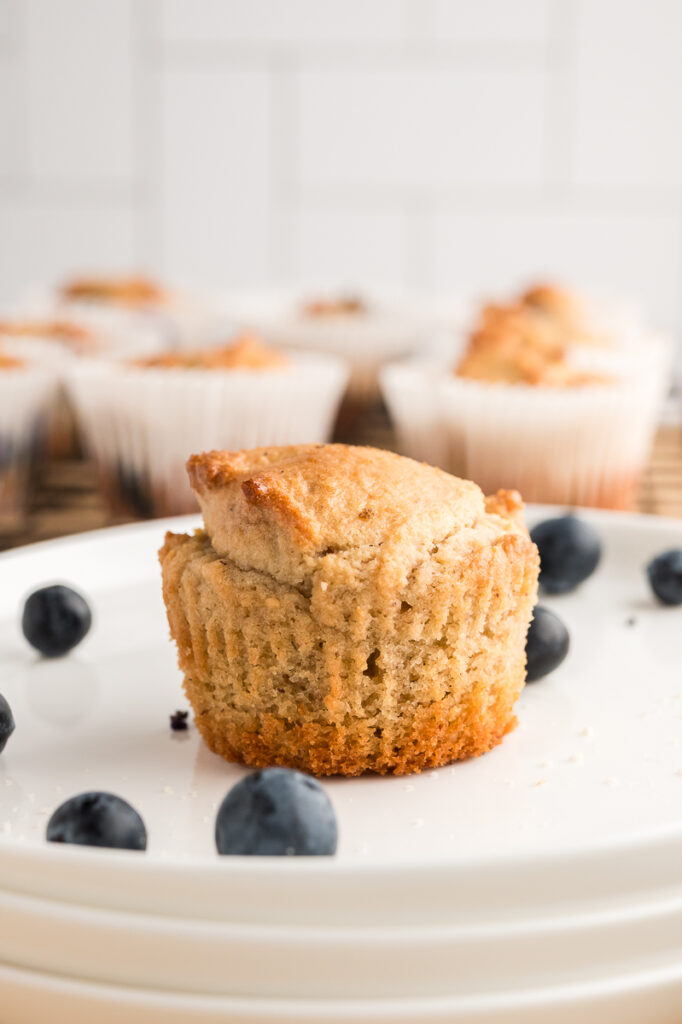 Almond flour muffin on a white plate with fresh blueberries and more muffins in the background