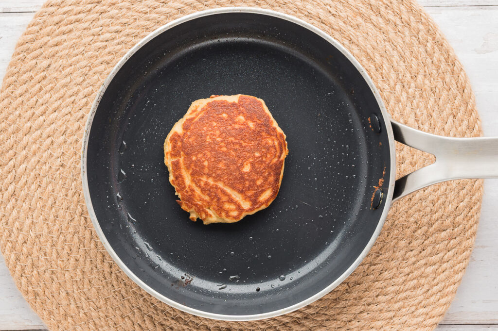 Almond flour pancake being flipped in a skillet showing golden brown underside