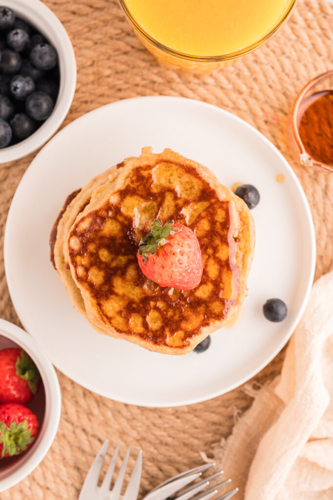 Overhead shot of almond flour pancakes on a white plate with maple syrup and fresh berries