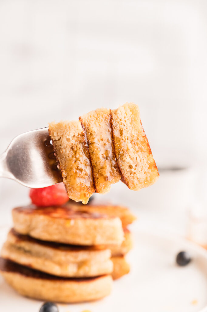 A fork lifting a fluffy gluten-free almond flour pancake with maple syrup
