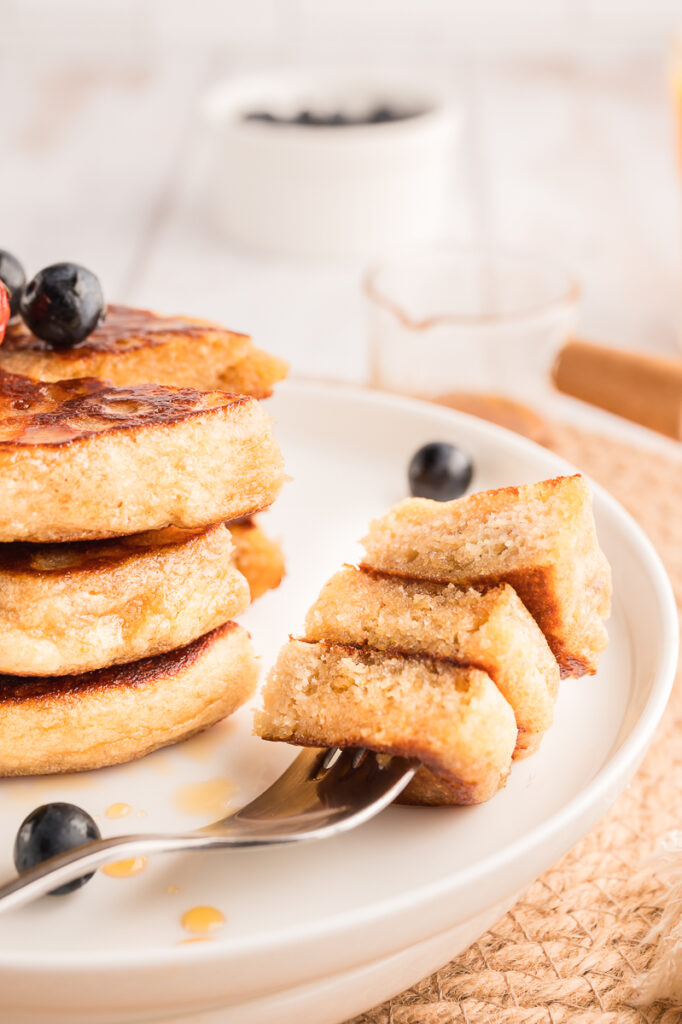 Almond flour pancakes plated with fresh fruit and a fork ready to eat