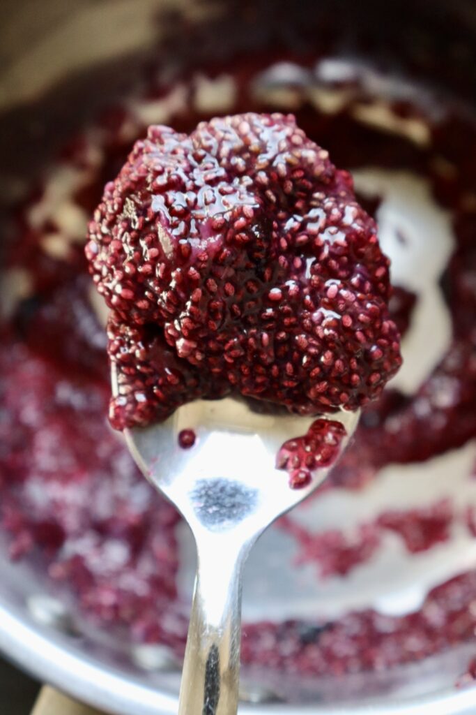 Close up of thick blueberry chia seed jam on a spoon, showing glossy texture and visible chia seeds