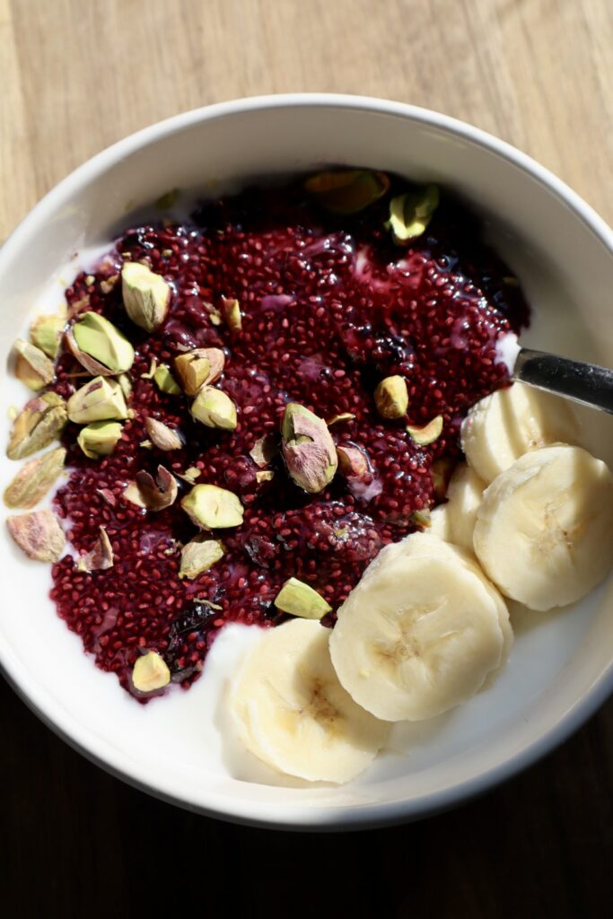 Finished blueberry chia yogurt bowl topped with sliced banana, chopped nuts, and a drizzle of honey