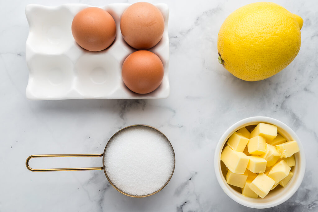 Lemon curd ingredients laid out: fresh lemons, eggs, butter, sugar, and a zester.