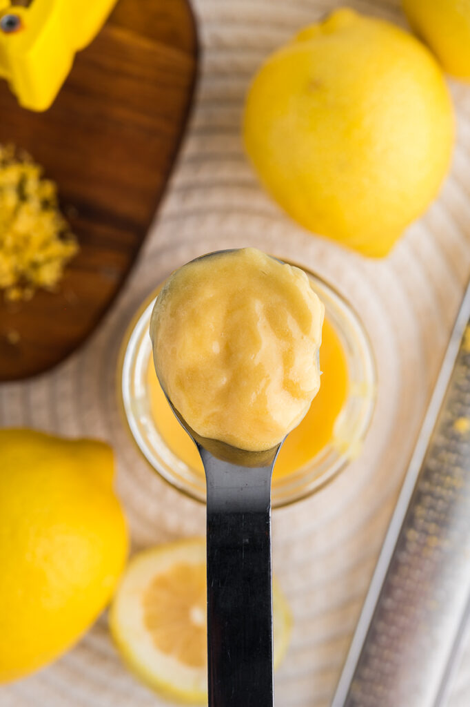 Glossy lemon curd dripping off a spoon into a small bowl.