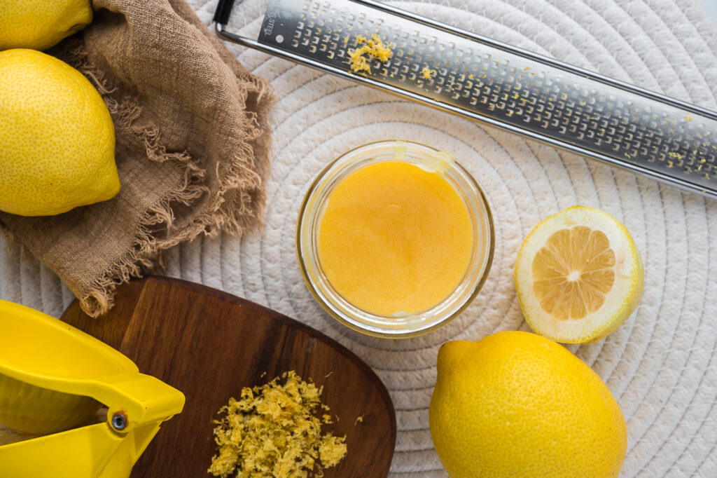 A jar of homemade lemon curd next to a citrus juicer and zester on a kitchen counter.