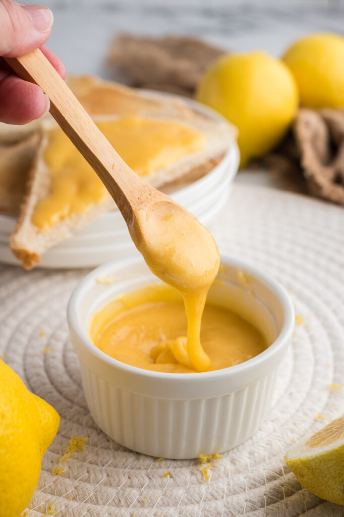 A spoon lifting silky homemade lemon curd from a small white ramekin.