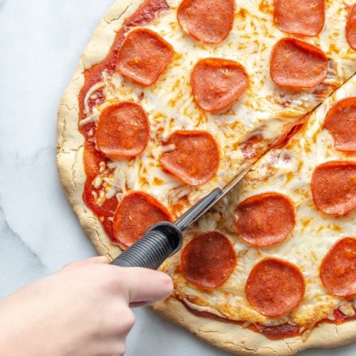 hand cutting Gluten-Free Pizza topped with cheese and pepperoni